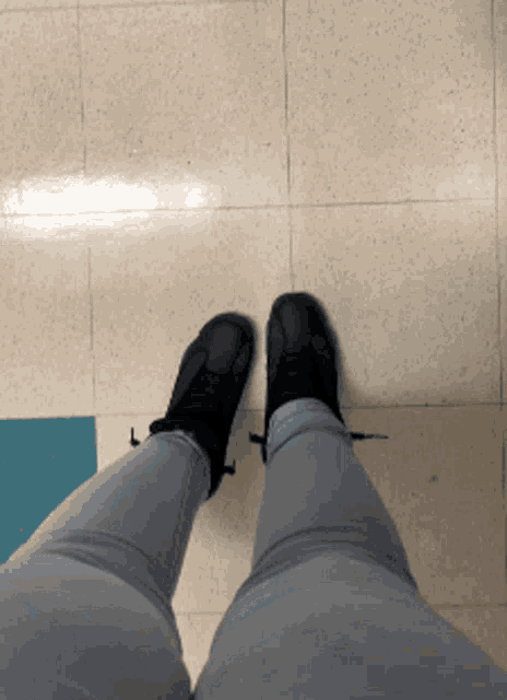 a person wearing a pair of black shoes standing on a tile floor