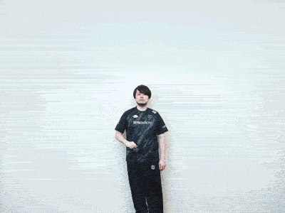 a man in a black shirt with the word zeta on it stands in front of a white wall