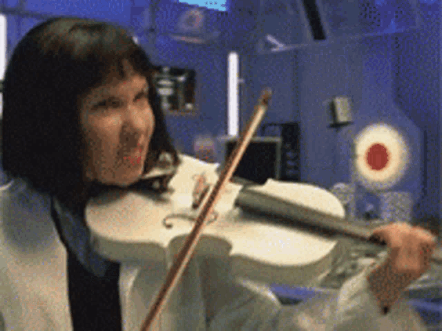 a woman is playing a violin in a room with a target in the background