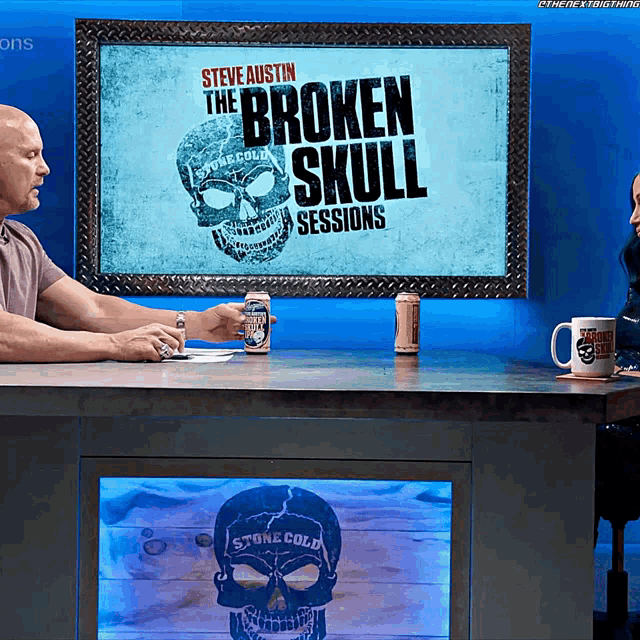 two men sit at a table in front of a screen that says broken skull sessions