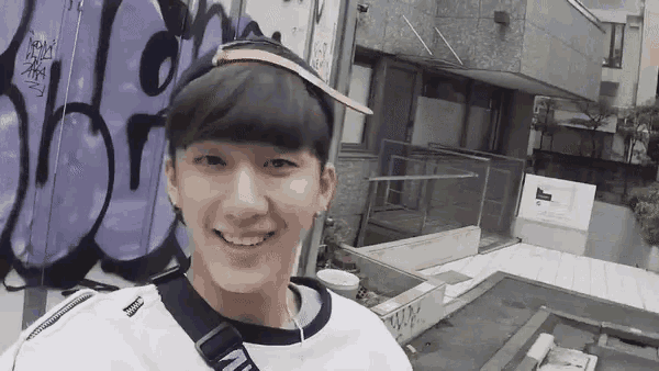 a young man wearing a headband and sunglasses smiles in front of a building with graffiti on it .