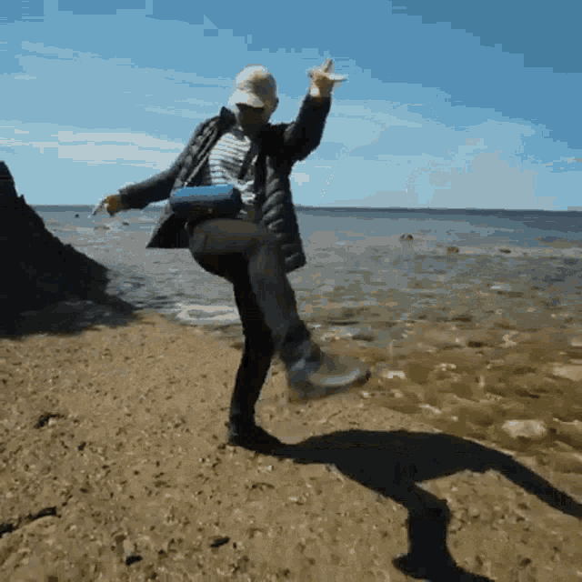 a person standing on one leg on a beach with their arms in the air