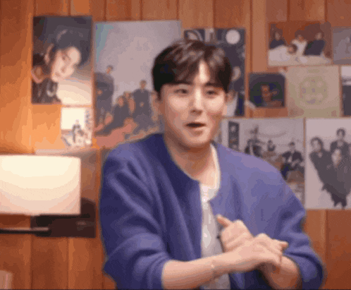 a man in a blue sweater is clapping his hands in front of a wall with pictures on it .
