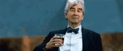 an older man in a suit and bow tie is holding a glass of whiskey .
