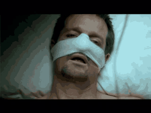 a man is laying in a hospital bed with a bandage on his nose