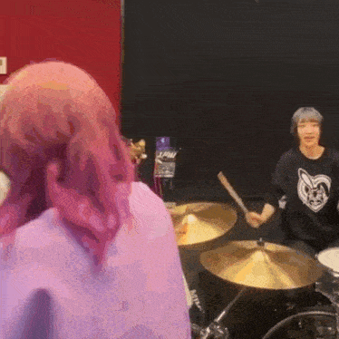 a woman with pink hair is playing drums in front of a man playing drums .