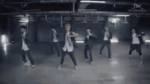 a group of young men are dancing in a dark room with a sm logo in the background