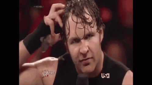 a man is scratching his head while standing in front of a microphone in a wrestling match .