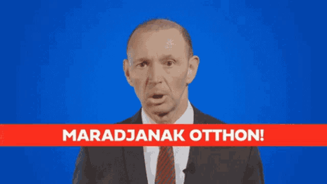 a man in a suit and tie stands in front of a blue background with the words maradjanak otthon