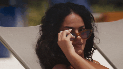 a woman wearing sunglasses sits in a chair with her hand on her eye