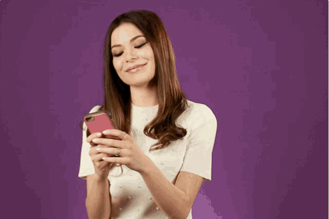 a woman in a white shirt is holding a cell phone in her hands