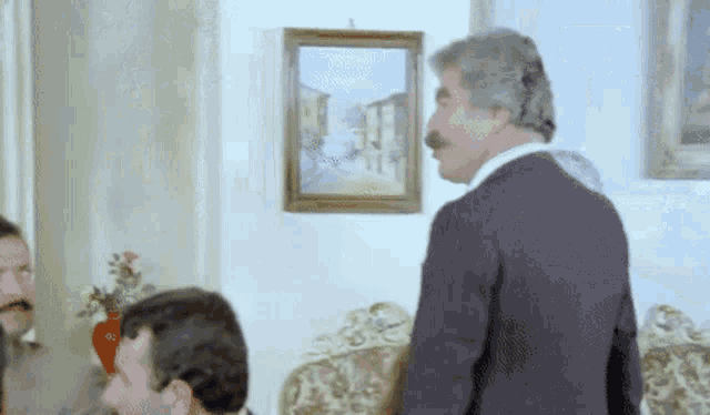 a man with a mustache is standing in a living room next to a couch .