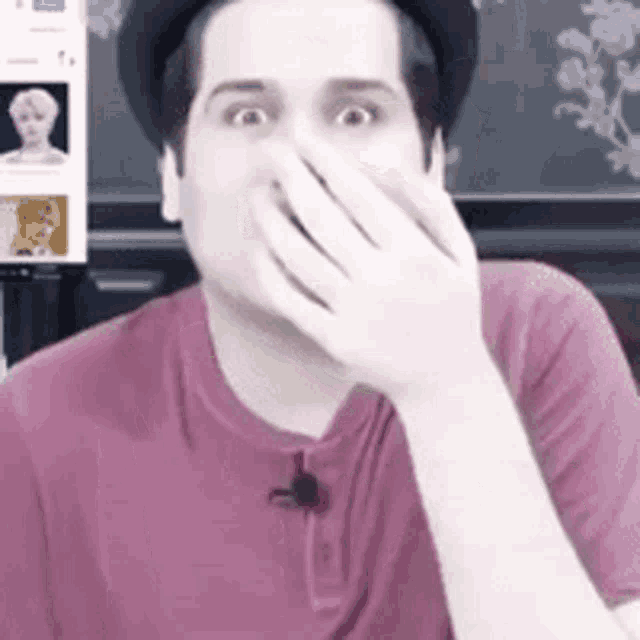 a man wearing a hat and a pink shirt is covering his face with his hand