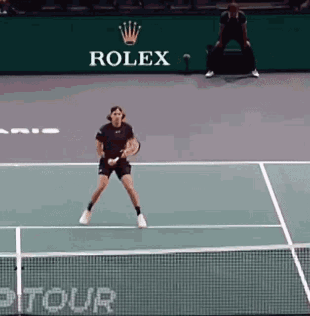 a man is playing tennis on a tennis court with a rolex logo on the wall behind him .