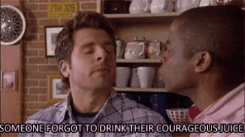 two men drinking their courageous juice in front of a brick wall .