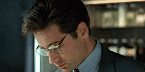 a man in a suit and tie is wearing glasses and looking down .