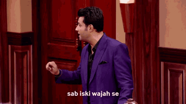 a man in a purple suit and black shirt is standing in front of a wooden door .