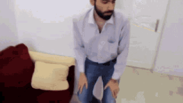 a man with a beard is kneeling down in a living room with his hands on his knees .
