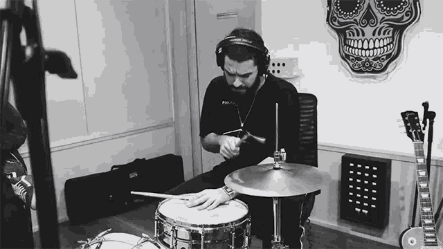 a man wearing headphones is playing drums in a room with a skull on the wall
