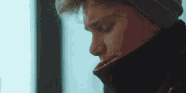 a young man wearing a hat and a scarf is looking down .