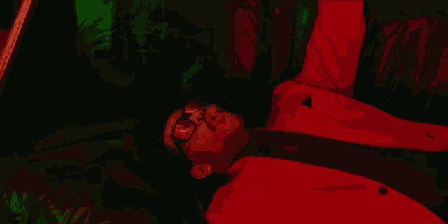 a man in a red suit and sunglasses is laying down in a dark room