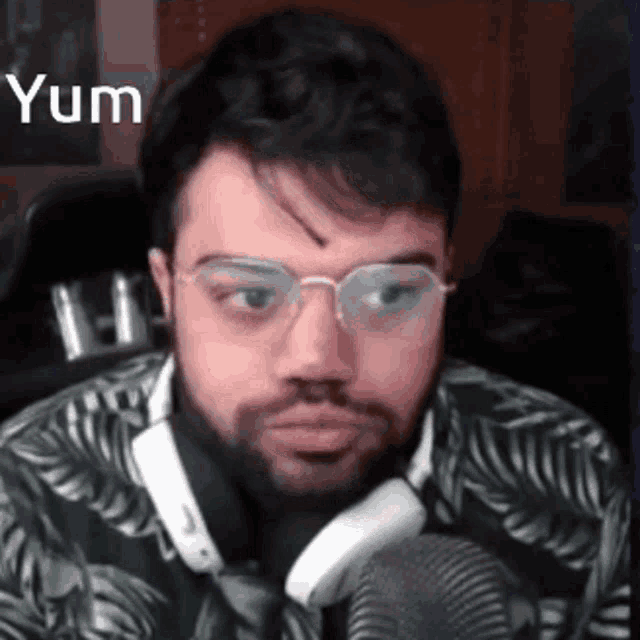 a man with a beard and glasses is sitting in front of a microphone and making a funny face .