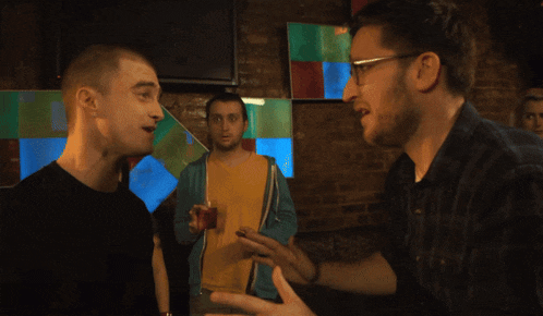 a man wearing glasses talks to another man in a bar
