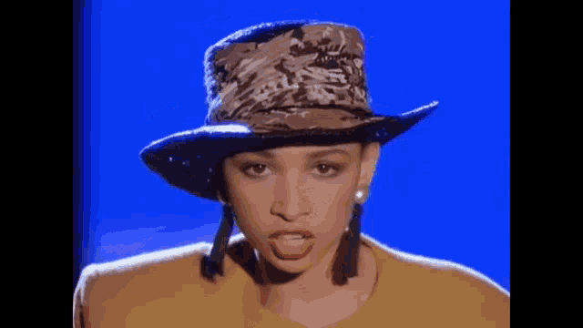 a woman wearing a hat and earrings is standing in front of a blue screen .