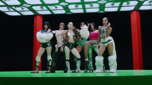 a group of women are standing on a green stage with a black background