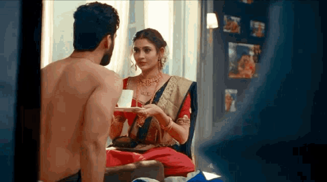 a shirtless man and a woman are sitting on a bed . the woman is holding a cup of tea .