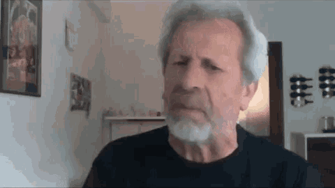a man with gray hair and a beard is sitting in a living room .