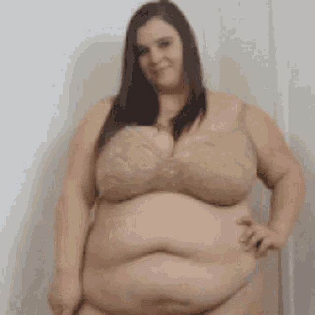 a woman with a very large belly is wearing a bra and standing in front of a white wall .