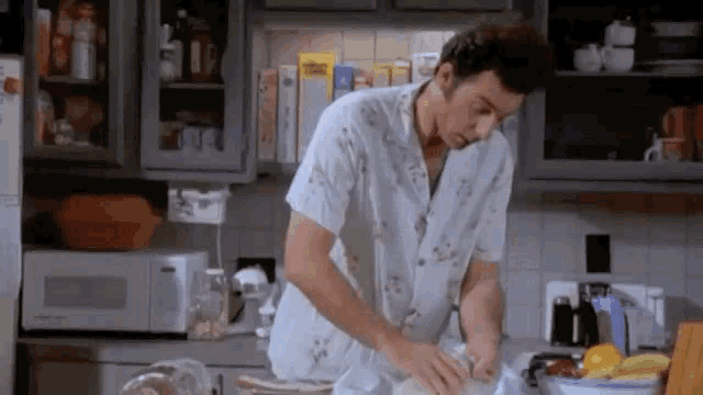 a man is kneading dough in a kitchen while wearing a white shirt .