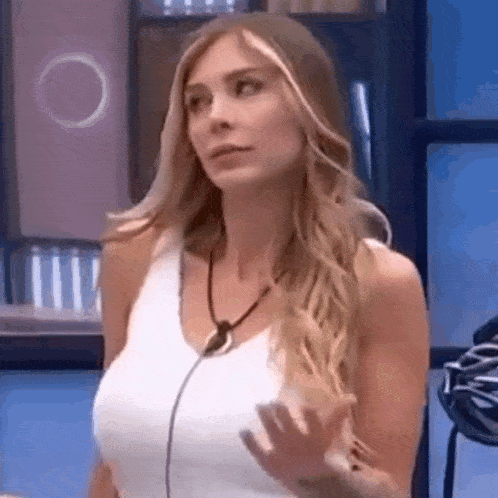 a woman in a white tank top is standing in front of a microphone and making a funny face .