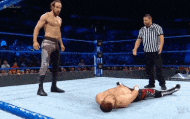 a referee is standing next to a wrestler laying on the ground