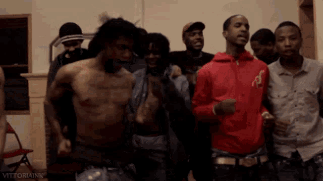 a shirtless man in a red jacket is surrounded by a group of men