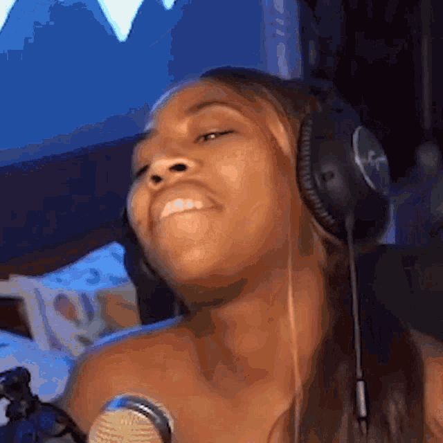 a woman is wearing headphones and smiling in front of a microphone .