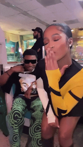 a woman in a yellow and black outfit kisses a man in sunglasses