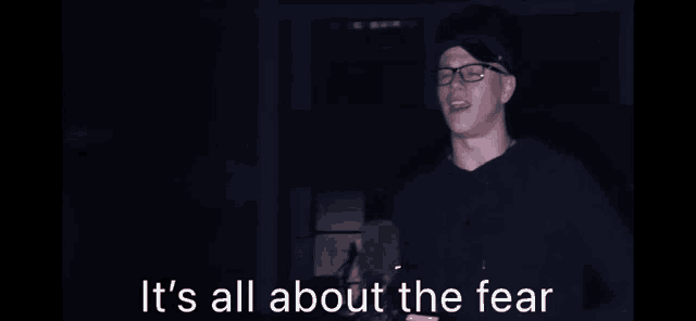 a man with glasses and a blindfold says it 's all about the fear while holding a gun