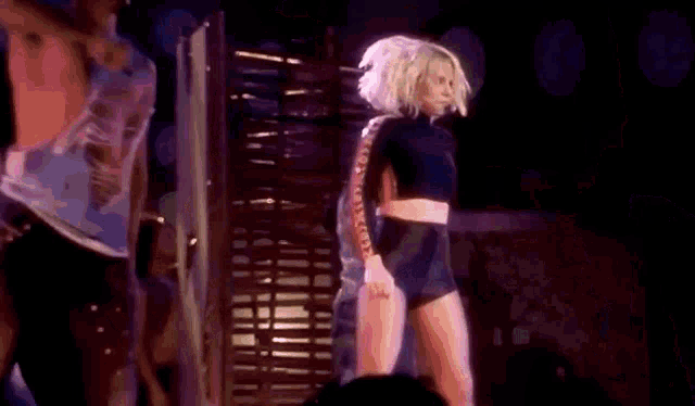 a woman is dancing on a stage in front of a crowd while a man stands behind her .