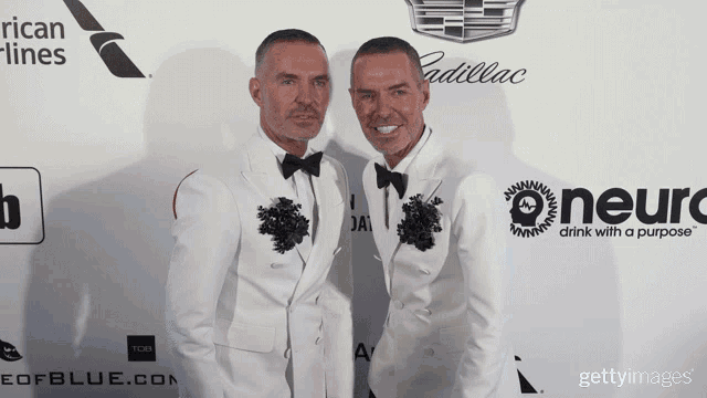 two men in white tuxedos pose for a photo in front of a cadillac sign