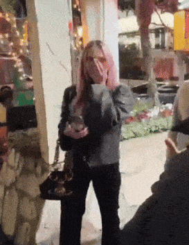 a woman with pink hair is covering her face with her hands
