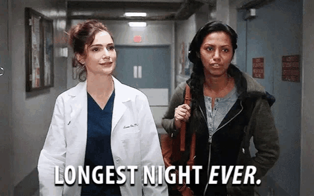 two women are walking down a hospital hallway and one of them is holding a purse .