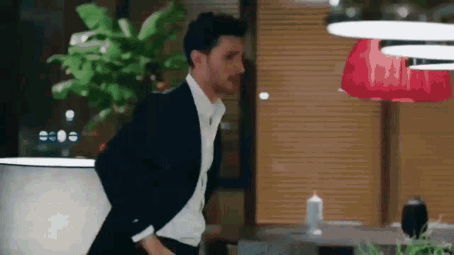 a man in a suit and white shirt is standing in front of a red lamp .