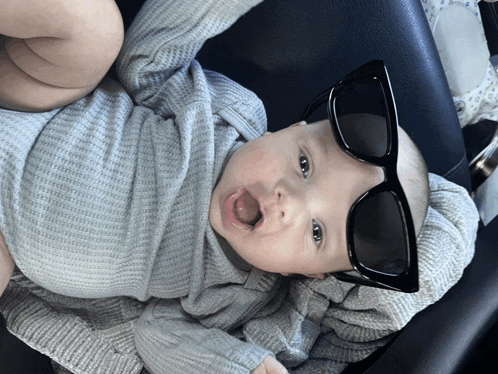 a baby wearing sunglasses and a grey sweater is laying down