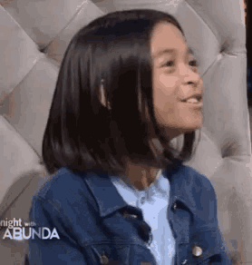 a young girl wearing a denim jacket is sitting in a chair and smiling
