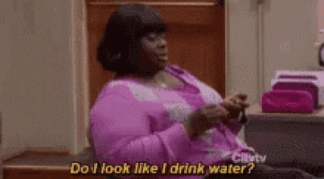 a woman in a pink shirt is sitting at a desk holding a glass of water .