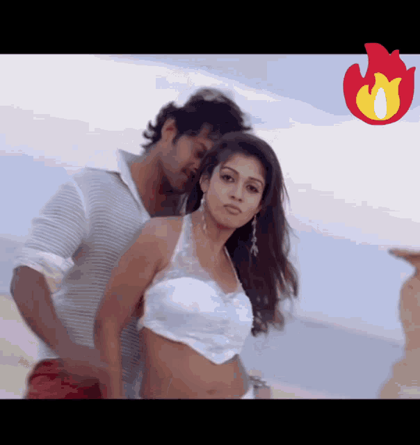 a man and a woman are dancing on a beach with a fire icon in the corner