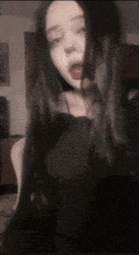 a woman with long black hair is taking a selfie with her tongue out .