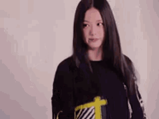 a woman in a black sweater is standing in front of a white wall and looking at the camera .